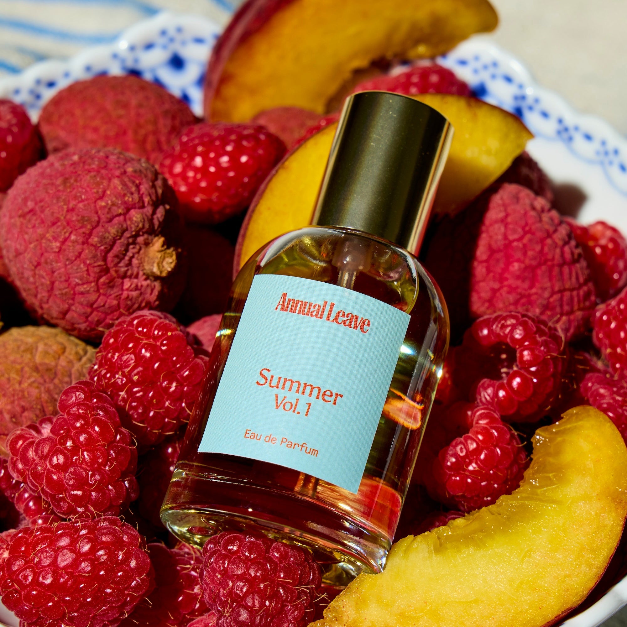 Perfume bottle labeled 'Annual Leave Summer Vol. 1' on a bed of raspberries and peaches.