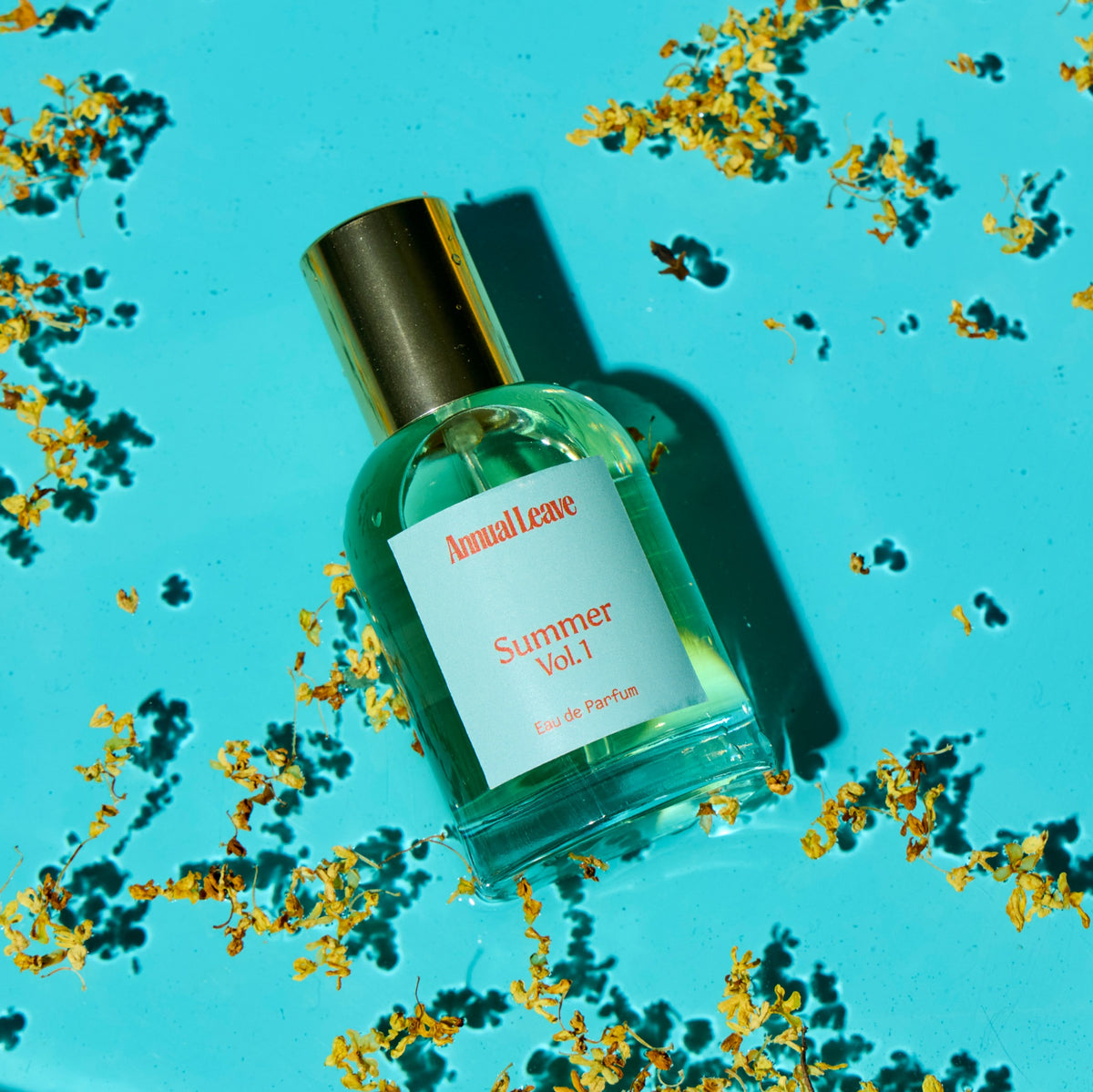 Perfume bottle labeled 'Summer Vol. 1' by Annual Leave on a blue background with scattered osmanthus flowers.