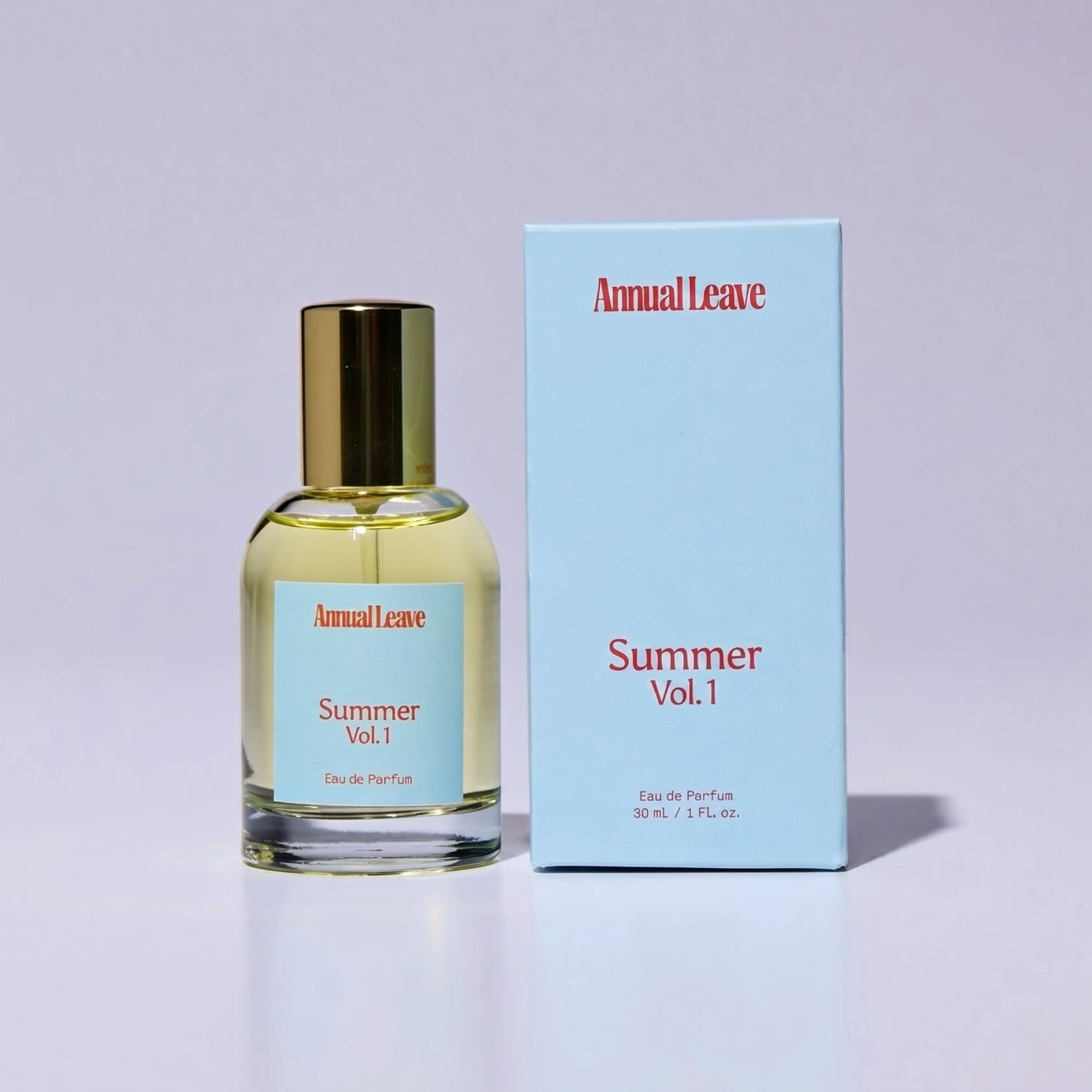 A bottle of Annual Leave Summer Vol.1 Eau de Parfum with a gold cap next to its light blue packaging box, set against a clean light purple background.